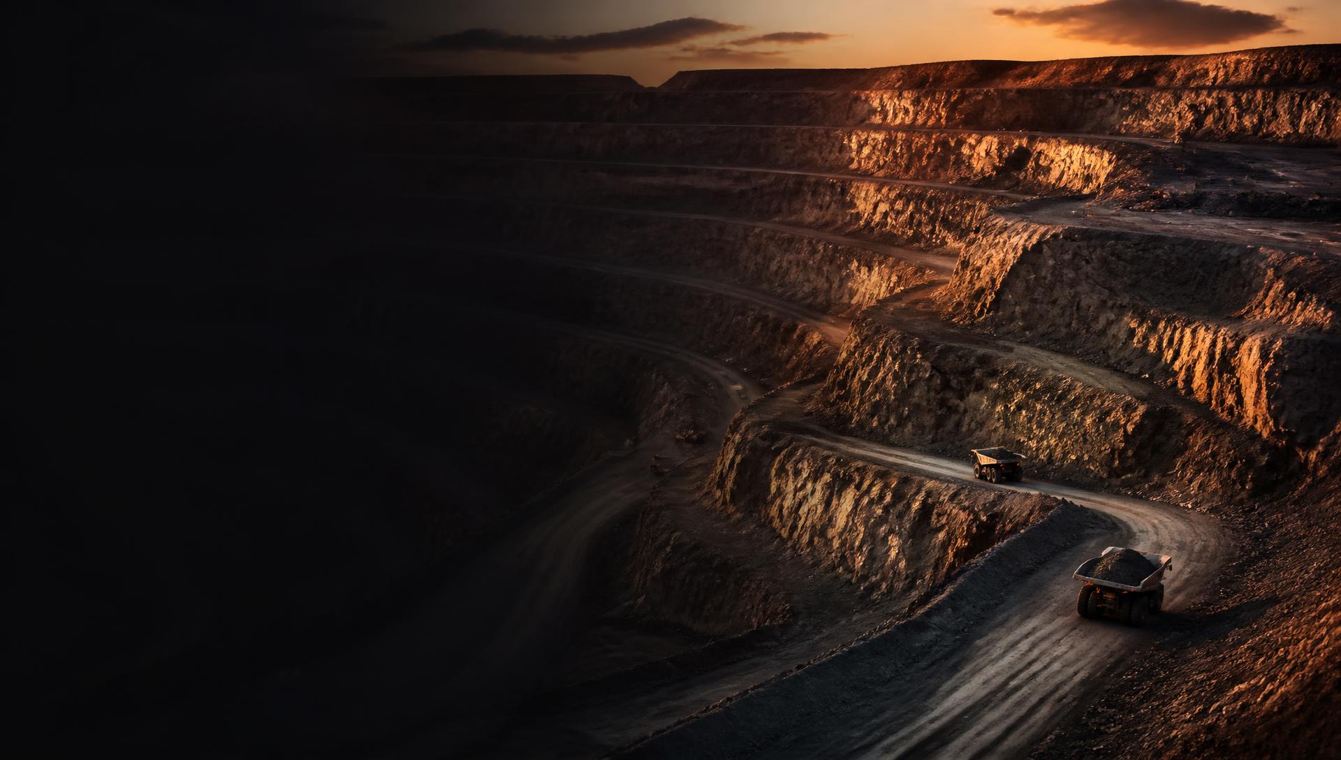 Open-pit mine at dusk with haul trucks on terraced benches
